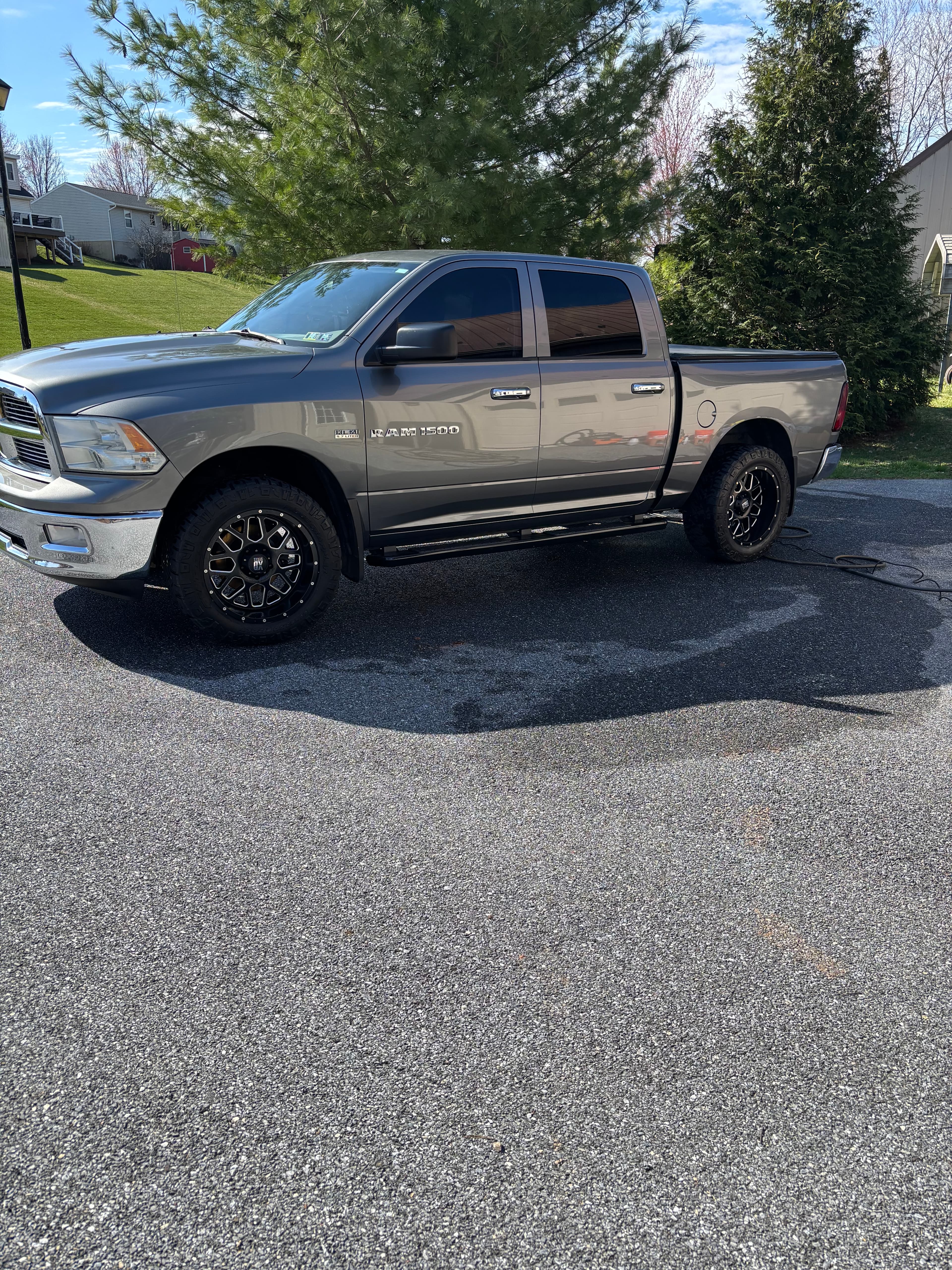 Gray Ram 1500 pickup truck with custom black wheels parked on a wet driveway.