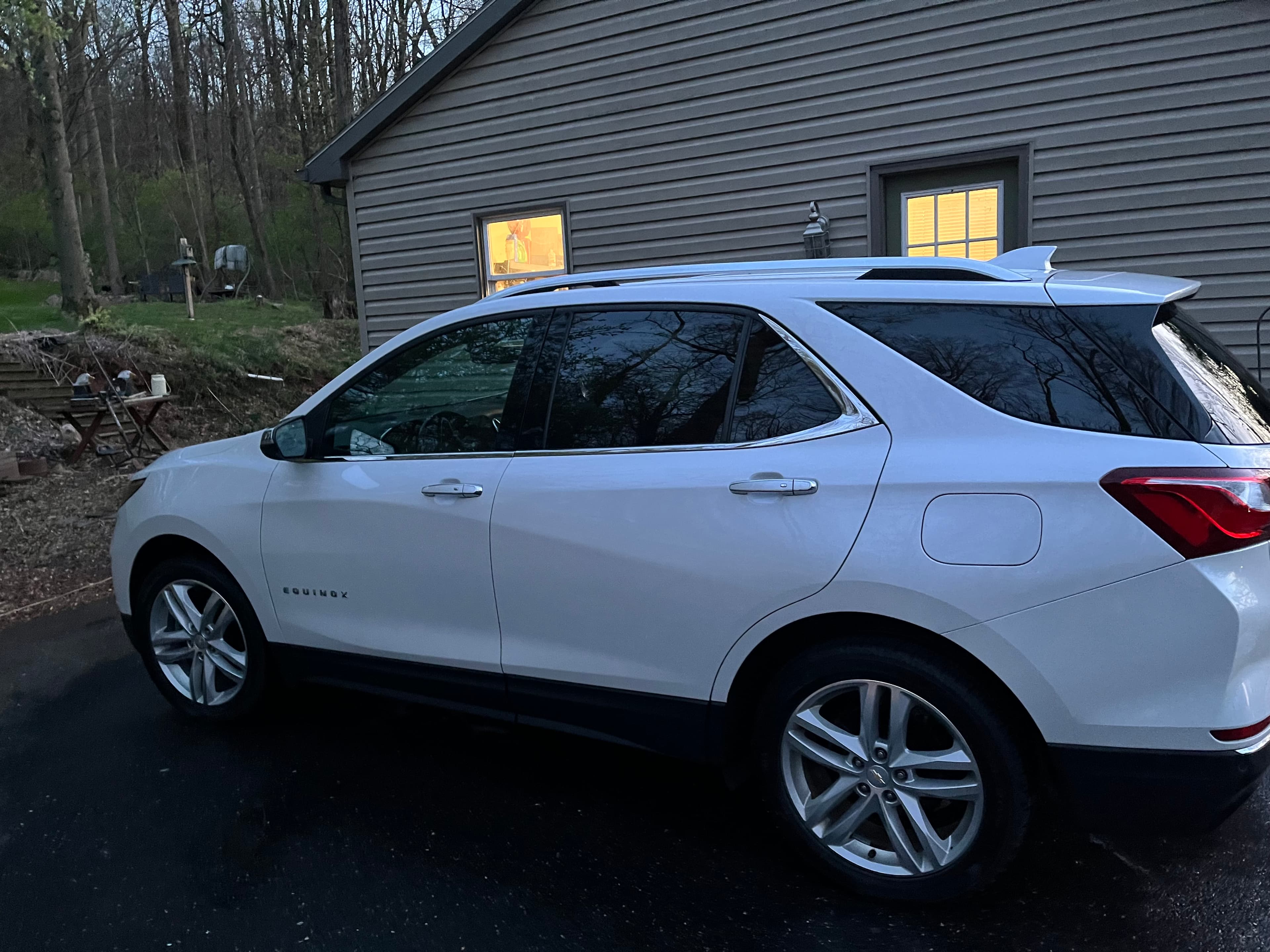 White Chevrolet Equinox SUV parked on a driveway next to a gray house at twilight.
