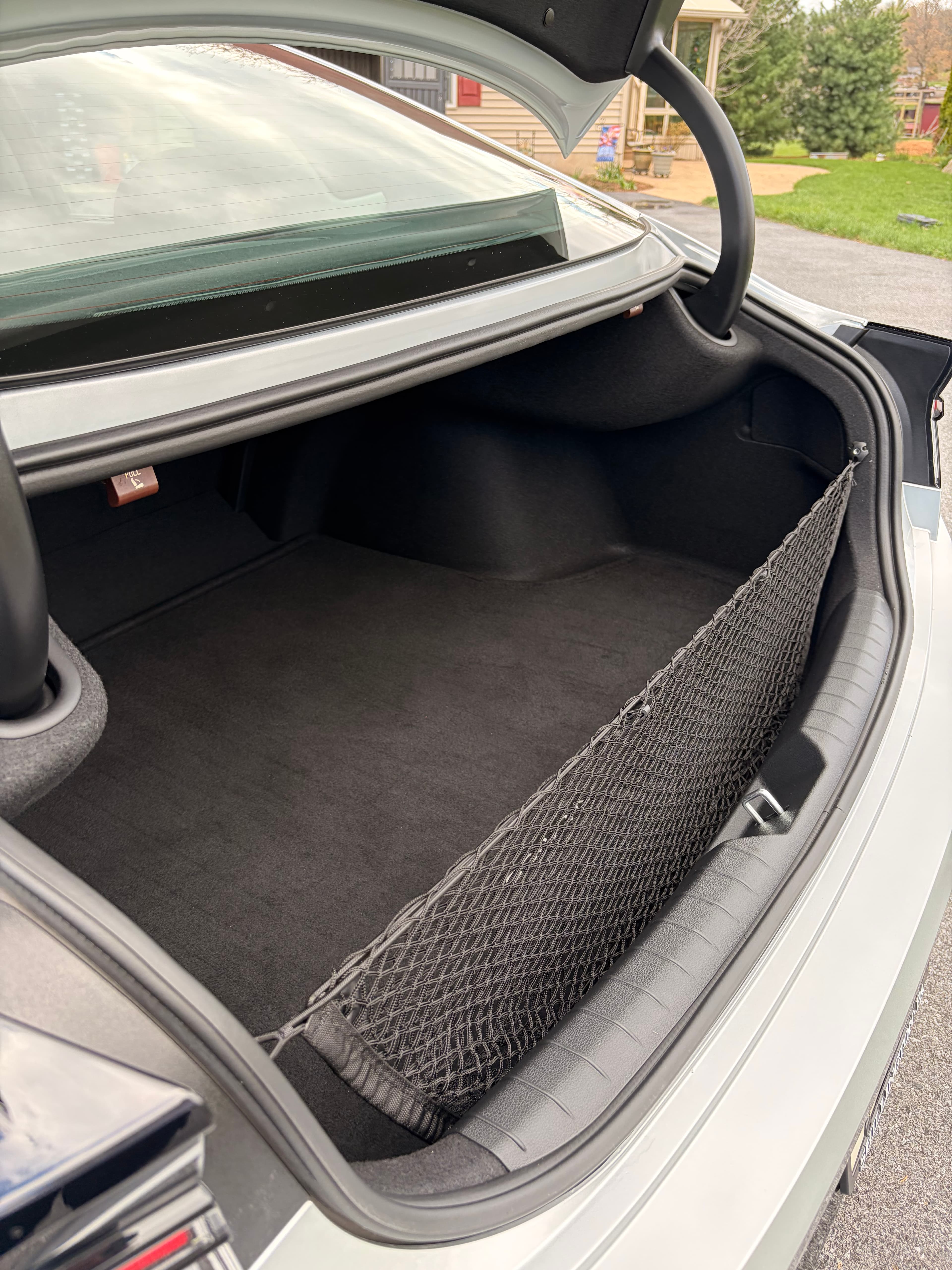 Open silver car trunk showing a black carpeted interior and a mesh cargo net.